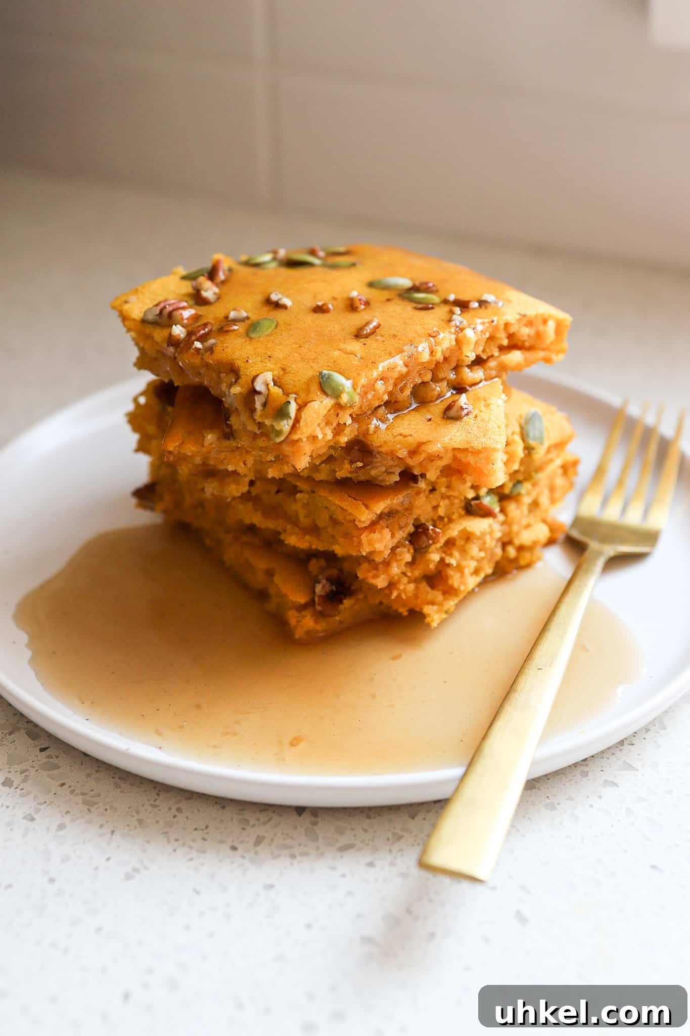 Baked Pumpkin Sheet Pan Pancakes — Fluffy Fall Brunch Recipe 2 side angle of fluffy pumpkin sheet pan pancakes stacked on top of one another on a white plate with gold fork