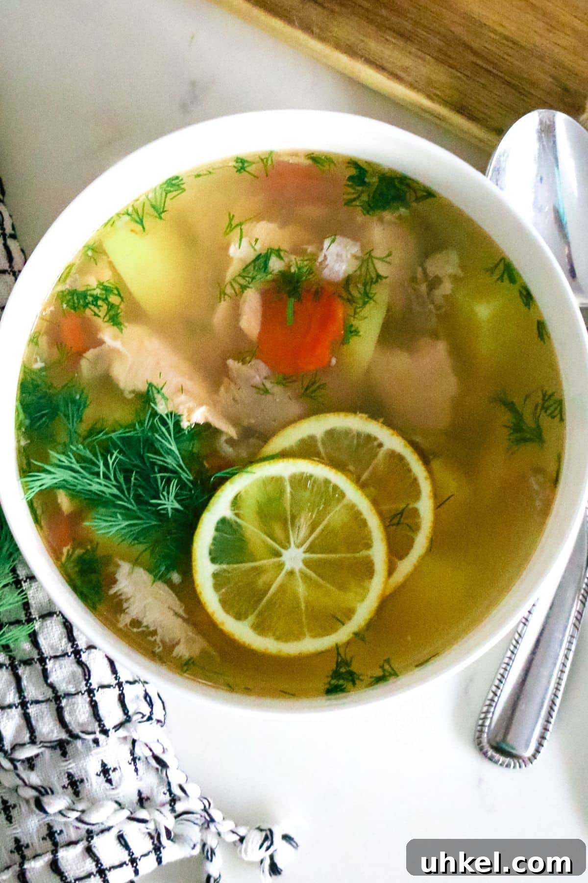 Authentic Ukha Fish Soup Recipe: Clear Russian Fisherman’s Broth 2 fish soup in a white bowl next to a towel a spoon and a cutting board.