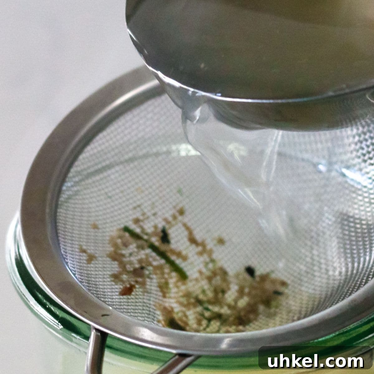 Authentic Ukha Fish Soup Recipe: Clear Russian Fisherman’s Broth 8 metal ladle pouring fish stock into strainer over a glass jar