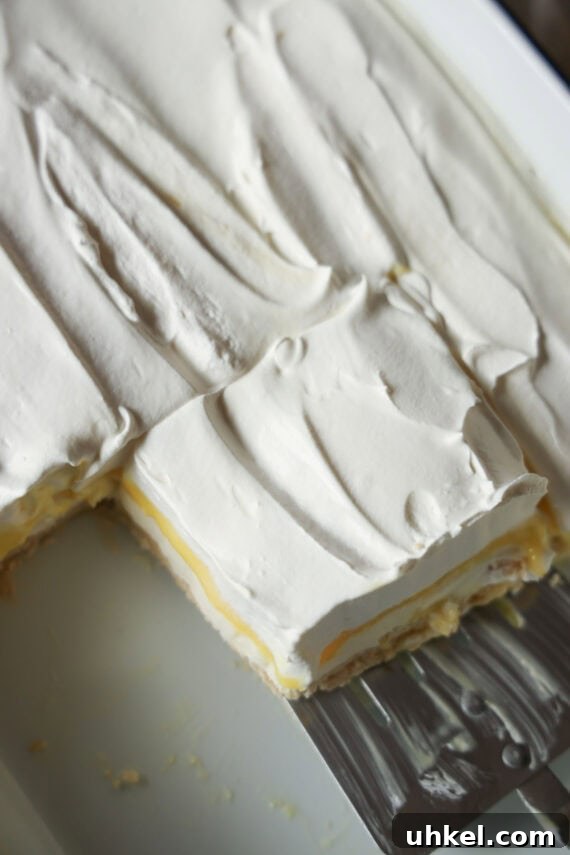Decadent Lemon Lush Dessert with Graham Cracker Crust 7 Serving a slice of Lemon Lush dessert out of a 9x13 pan with a spatula.