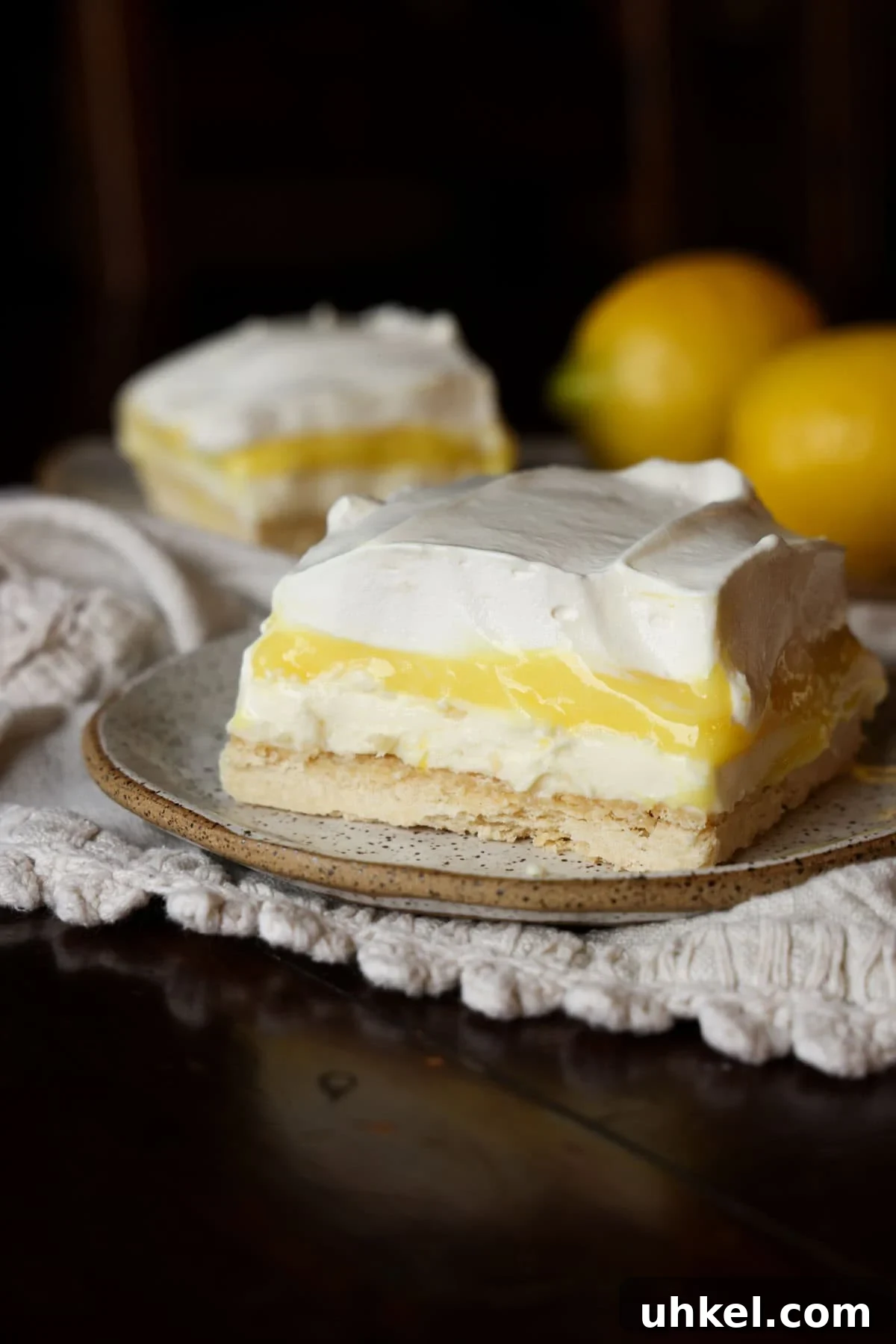 These super easy, nostalgic Lemon Lush is the perfect make-ahead dessert. Layers of creamy whipped topping, lemon pudding, and cheesecake all topped on the most delicious, buttery shortbread crust! A slice of lemon pudding lush on a plate with whipped cream topping.