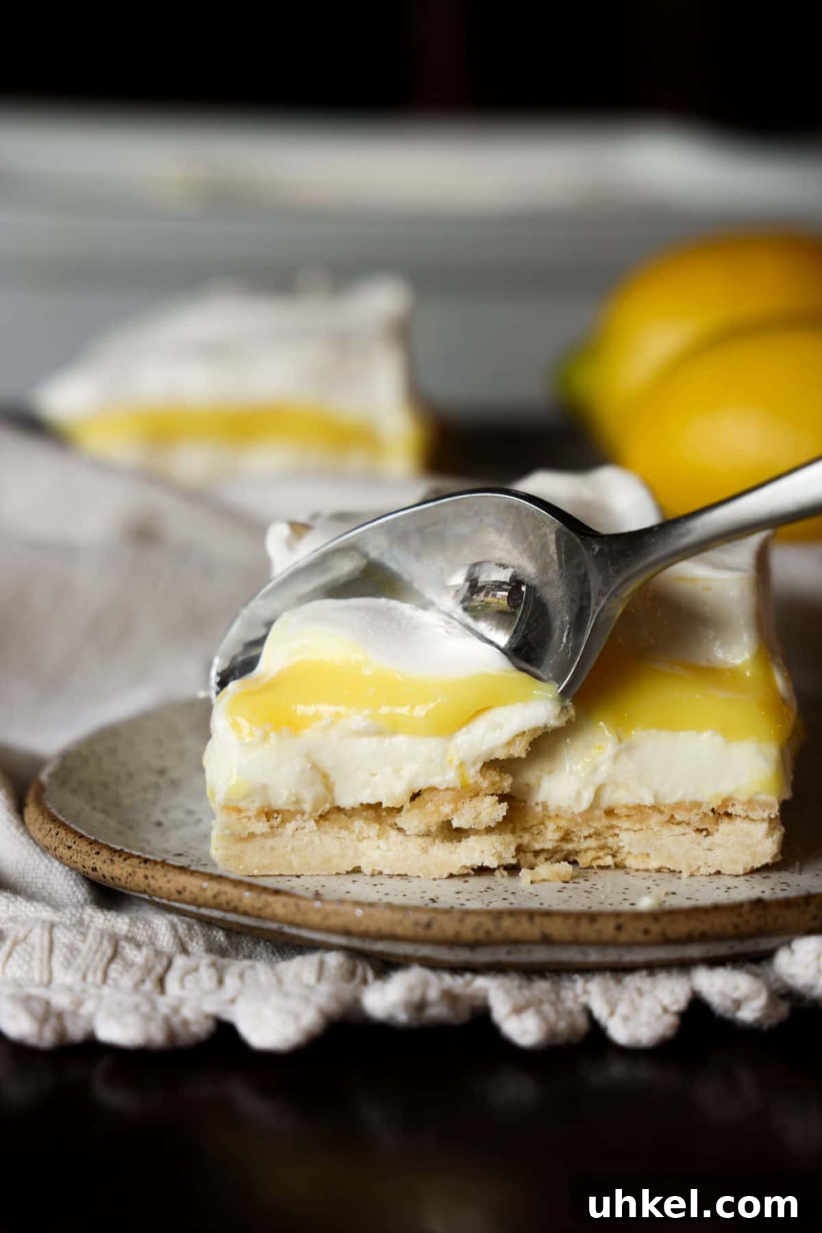 These super easy, nostalgic Lemon Lush is the perfect make-ahead dessert. Layers of creamy whipped topping, lemon pudding, and cheesecake all topped on the most delicious, buttery shortbread crust! A slice of Lemon Lush dessert on a plate with a spoon taking a piece of.
