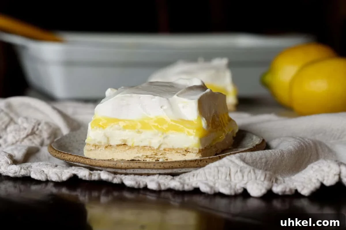These super easy, nostalgic Lemon Lush is the perfect make-ahead dessert. Layers of creamy whipped topping, lemon pudding, and cheesecake all topped on the most delicious, buttery shortbread crust! Lemon Delight Pudding dessert sliced on a plate