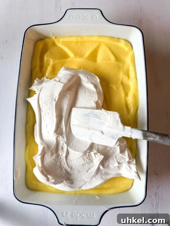 Decadent Lemon Lush Dessert with Graham Cracker Crust 6 Spreading whipped topping on top of lemon pudding in a 9x13 pan for a layered lemon dessert.