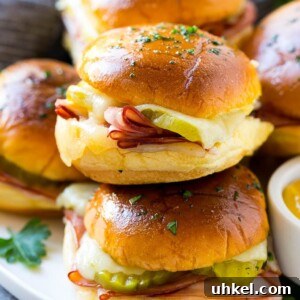A pile of cuban sliders filled with ham, cheese and pickles.