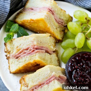 A plate of Monte Cristo sandwich with fresh fruit and raspberry jam for dipping.