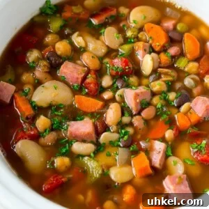 A slow cooker full of ham and bean soup made with vegetables, dried beans and diced ham.