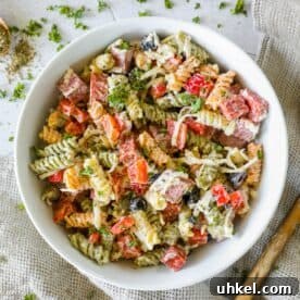 Creamy Italian Pasta Salad Recipe with Zesty Dressing and Veggies 10 A bowl of the best Italian pasta salad featuring tricolor rotini mixed with diced red bell peppers, black olives, chopped parsley, and shredded cheese, set on a textured cloth background.