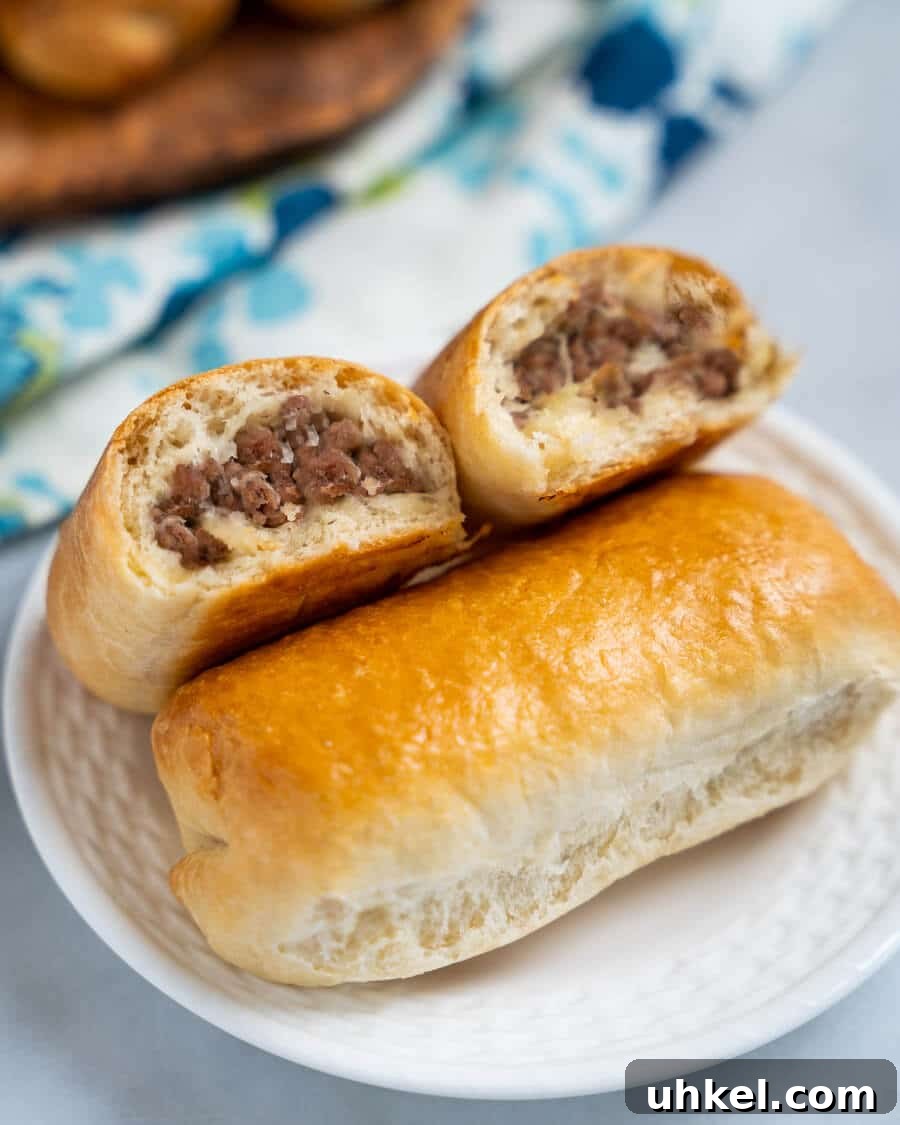 Ground Lamb Stuffed Buns Recipe – Savory Meat-Filled Bread 2 A meat bun cut in half showing cooked meat filling. The halves are leaning against a whole meat bun