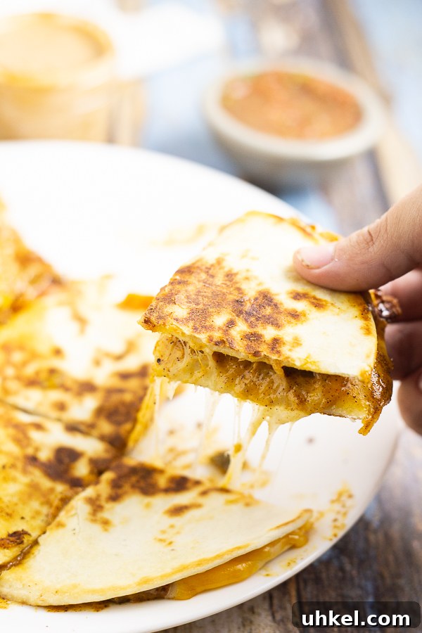Taco Bell Quesadilla Sauce Recipe (Copycat) 2 Hand picking up a quarter of a gooey, cheesy quesadilla from a white plate.