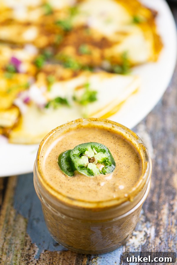 Taco Bell Quesadilla Sauce Recipe (Copycat) 3 Copycat Taco Bell Quesadilla Sauce in a small glass jar topped with 2 jalapeno slices with a quesadilla in the background.