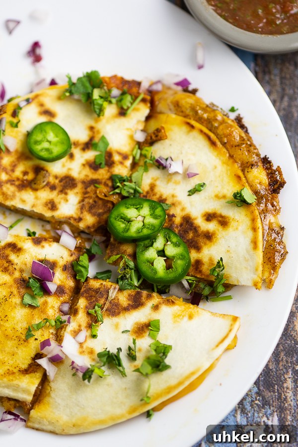 Taco Bell Quesadilla Sauce Recipe (Copycat) 4 Quesadilla on a white plate topped with fresh jalapeno slices, cilantro, and red onion on a white plate