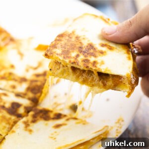 Taco Bell Quesadilla Sauce Recipe (Copycat) 5 Hand picking up a quarter of a gooey, cheesy quesadilla from a white plate.