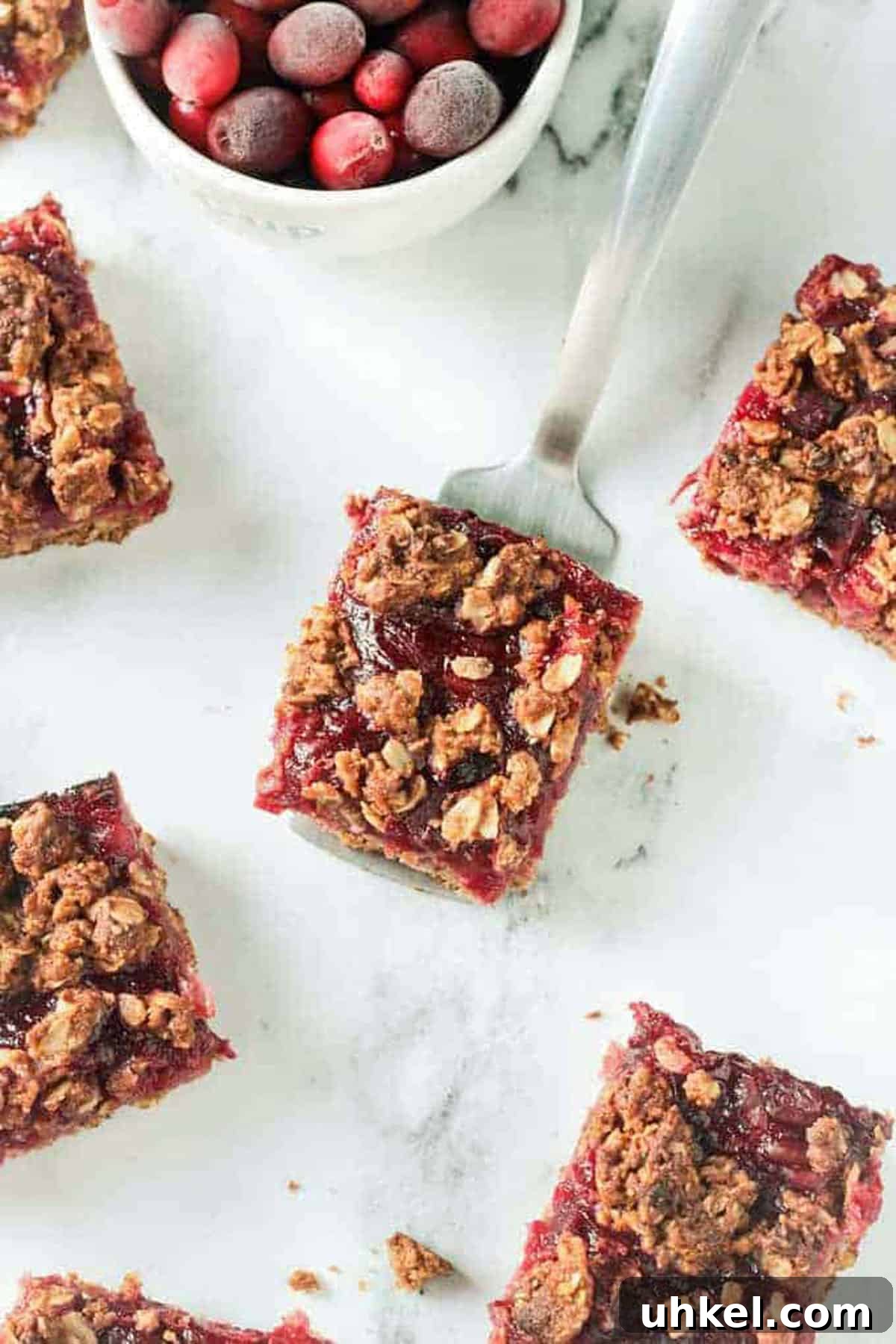 Cranberry Oatmeal Bars - sweet, tart, cranberry sauce nestled between a soft oatmeal base and a crumbly oat topping. One cranberry oat crumble bar on a metal spatula.