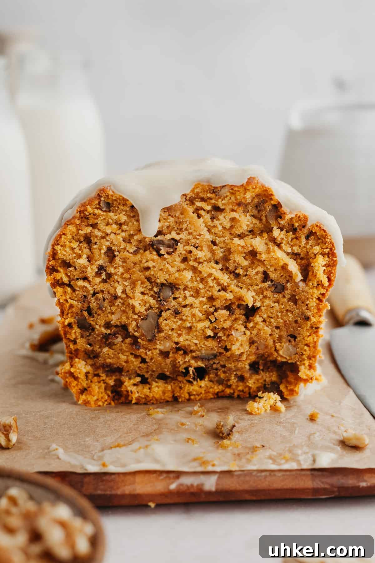 Maple-Glazed Pumpkin Walnut Bread Recipe 7 A pumpkin loaf with glaze on a cutting board.
