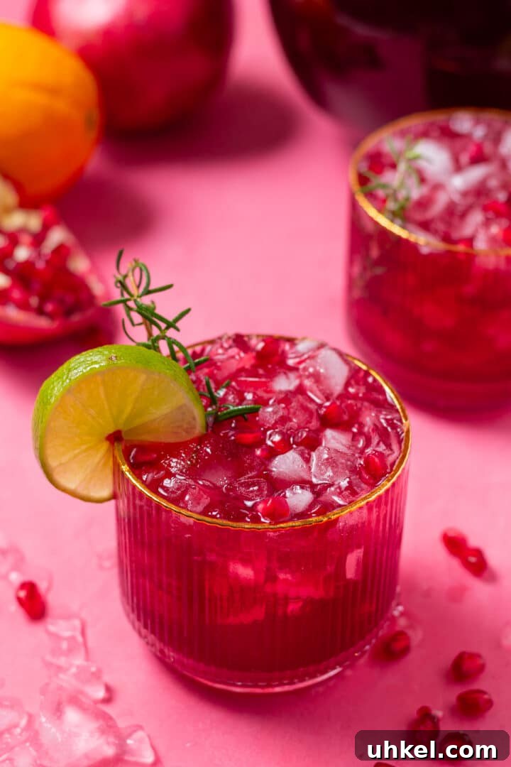 close up view of a glass with sparkly pomegranate punch, garnished with a sprig of rosemary and lime slice