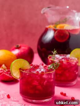 small tumbler with pomegranate punch garnished with lime and rosemary