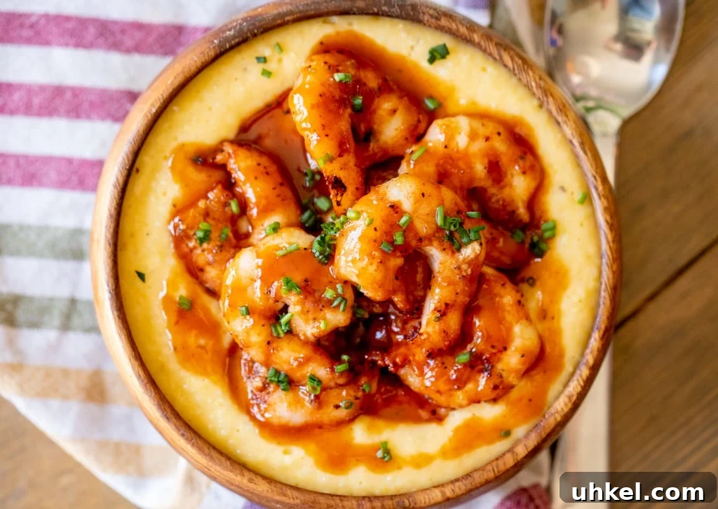 Grilled BBQ Shrimp with Creamy Southern Grits 4 Overhead view of a bowl full of grill shrimp and grits drizzled with sauce on top of a striped kitchen towel and next to a metal spoon.