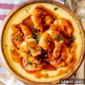 Overhead view of BBQ sauced shrimp on top of cheesy grits in a wooden bowl.
