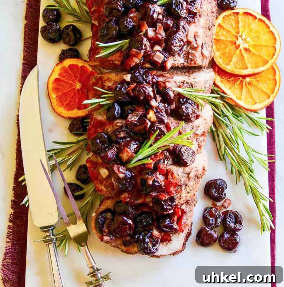 Carving fork and knife next to a pork loin roast topped with cherries.