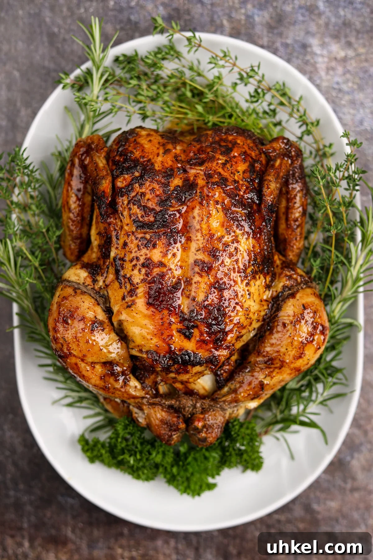 A roast chicken on a platter, surrounded by fresh herbs.