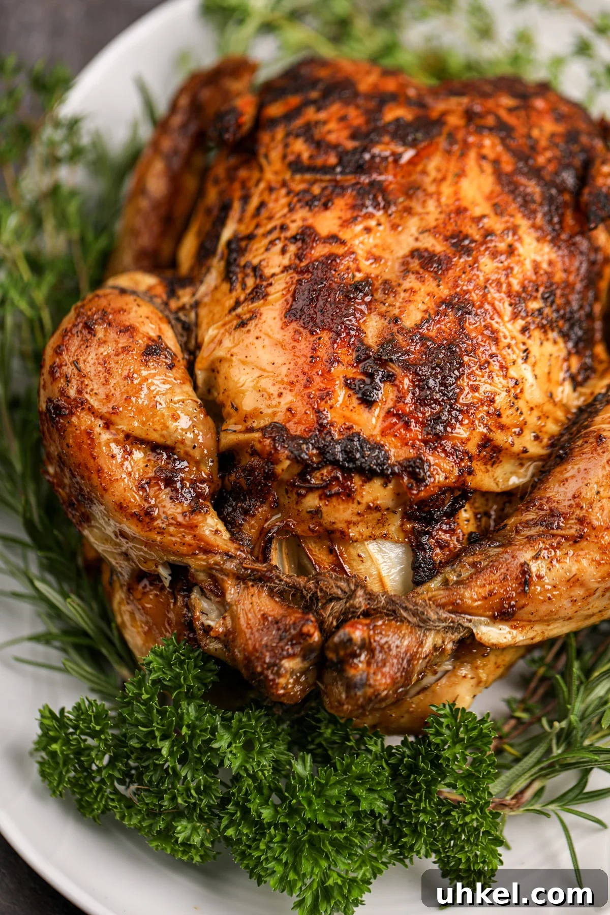 A whole roasted chicken on a platter garnished with herbs.