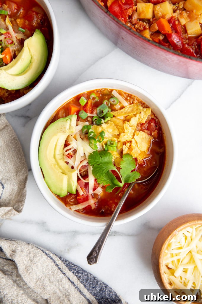 Hearty Vegan Quinoa Chili Recipe: Protein-Packed & Flavorful 2 Vegetable quinoa chili in a bowl, topped with cheese, avocado and crushed tortilla chips.