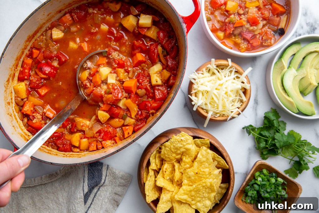 Hearty Vegan Quinoa Chili Recipe: Protein-Packed & Flavorful 12 The pot of chili on a countertop surrounded by toppings, including shredded cheese, avocado and tortilla chips.