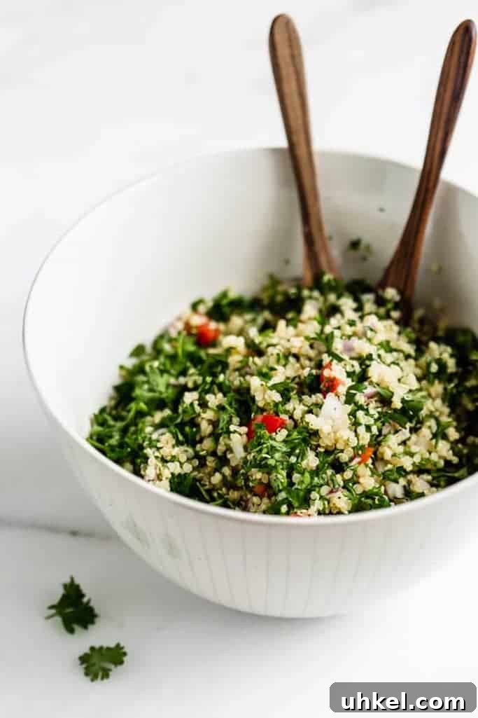 white mixing bowl filled with tabbouleh salad made with quinoa with two wooden spoons sticking out of the bowl