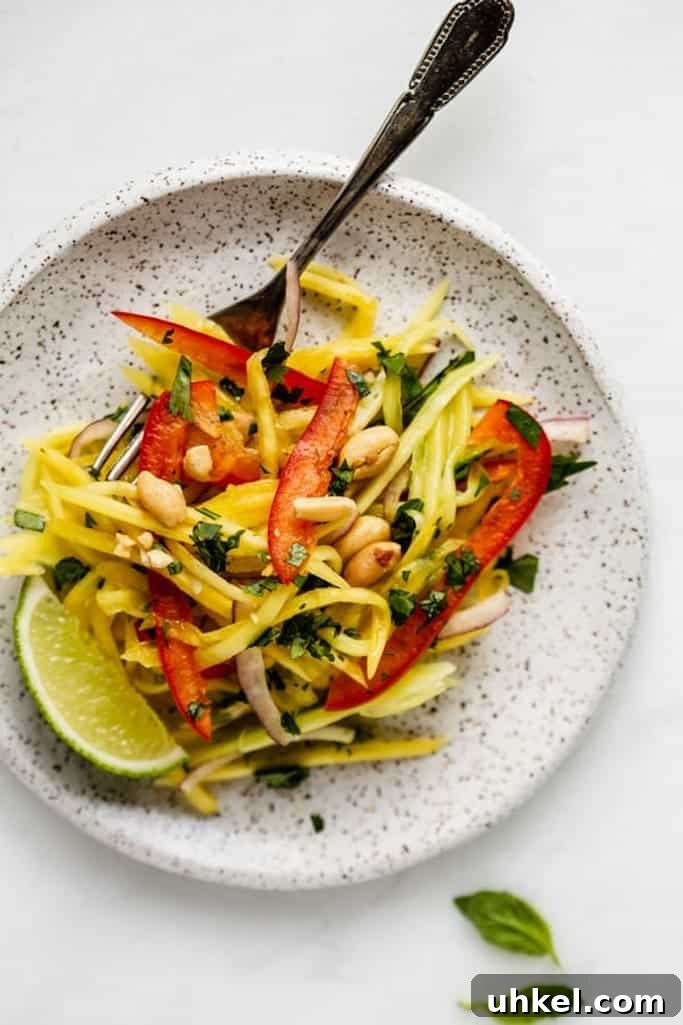 thinly sliced mango, red onion, and red pepper topped with roasted peanuts on a white speckled plate with a silver fork on a white marble table