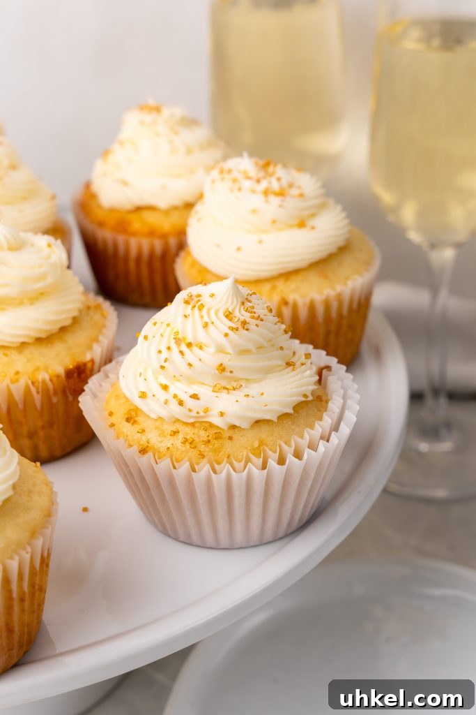 Champagne-Infused Cupcakes: Sparkling Celebration Recipe 2 champagne cupcakes on a white cake stand in front of flutes of champagne