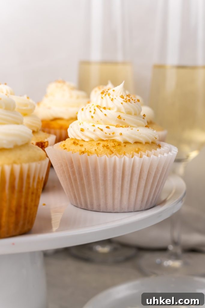 Champagne-Infused Cupcakes: Sparkling Celebration Recipe 11 champagne cupcakes on a white cake stand in front of flutes of champagne