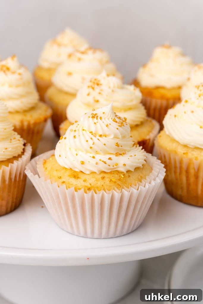 Champagne-Infused Cupcakes: Sparkling Celebration Recipe 3 gold sprinkle topped champagne cupcakes on a white cake stand