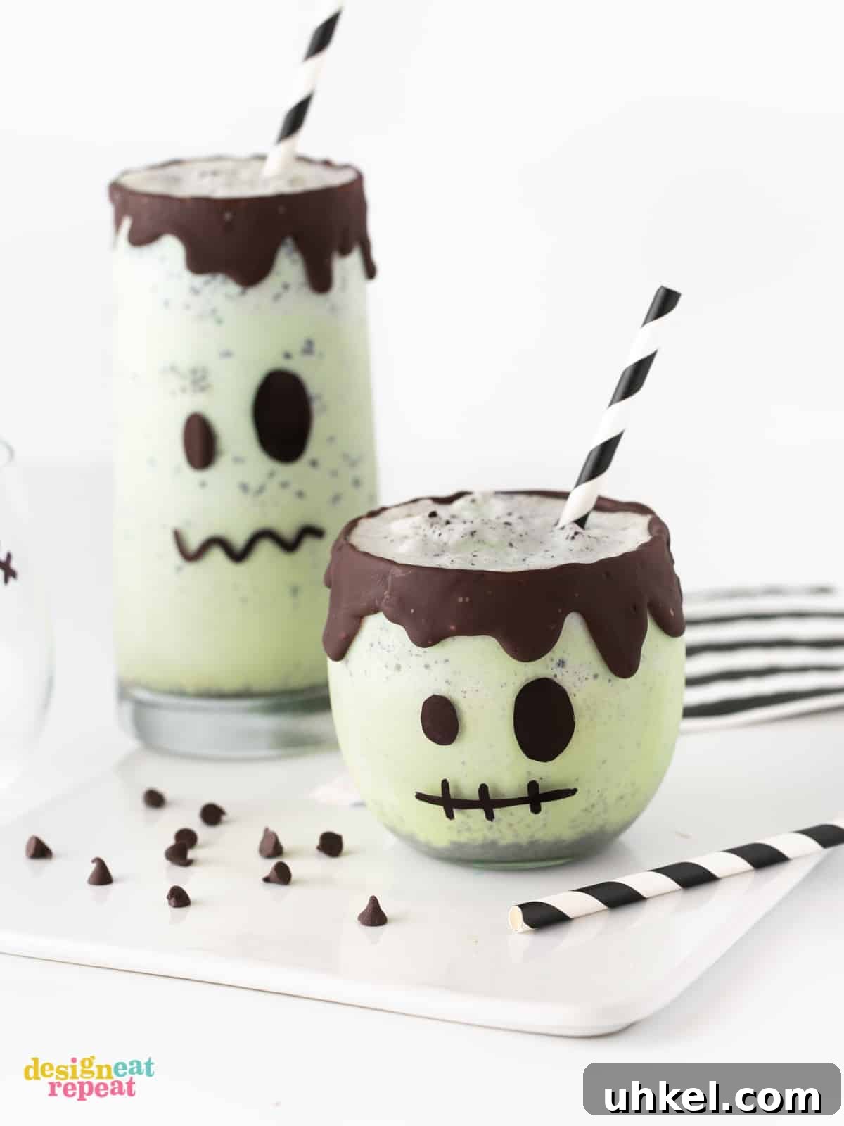 Frankenstein Halloween Milkshakes: Green Monster Dessert Recipe 6 Small mint milkshake decorated like Frankenstein with chocolate rim. With paper black straw and tall Frankenstein green milkshake on white cutting board. Easy Halloween Milkshakes.