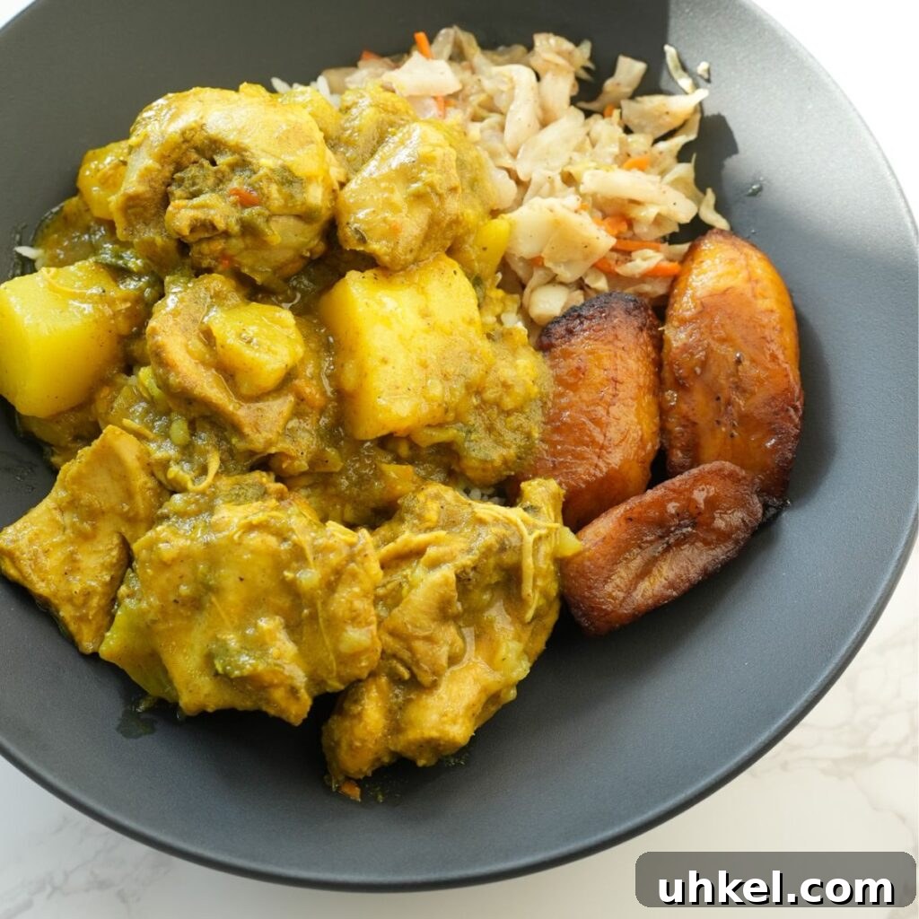 Authentic Jamaican Curry Chicken Recipe: Rich Island Flavor 10 Jamaican curry chicken on a black plate with plantain, cabbage and white rice.