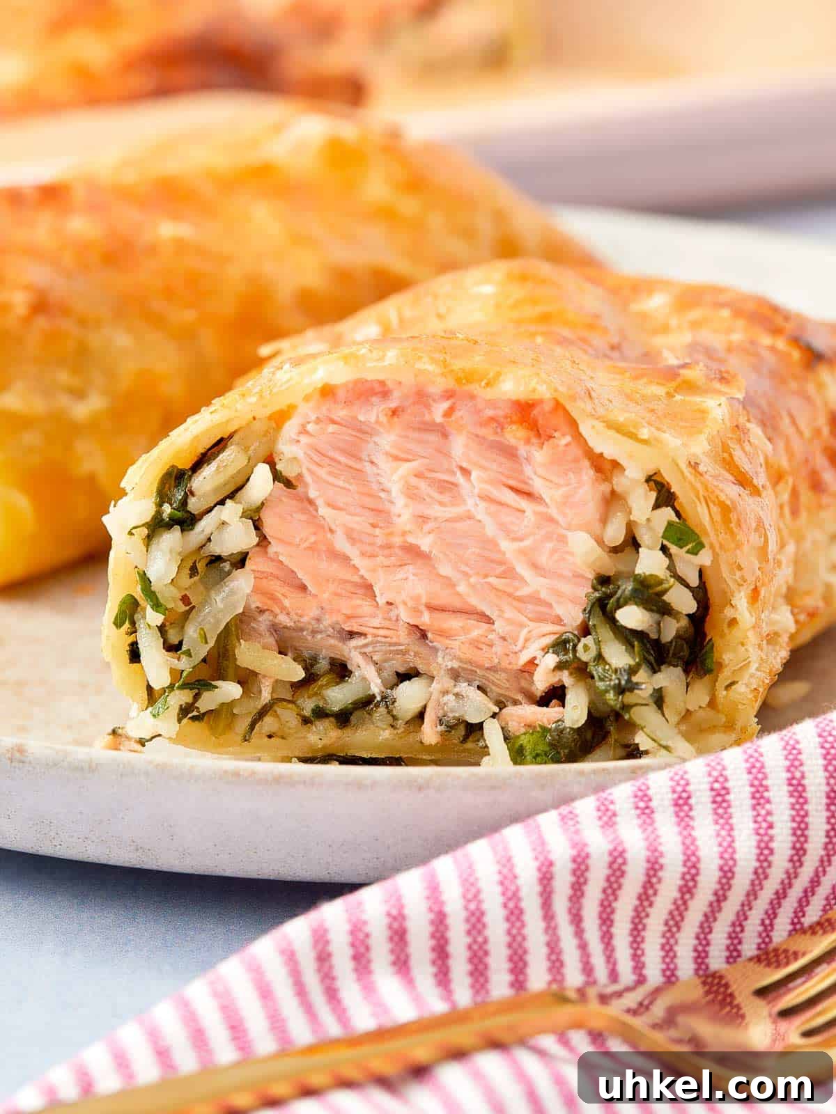 Close-up of a golden Puff Pastry Salmon Parcel sliced open to reveal flaky salmon, creamy spinach, and rice inside.