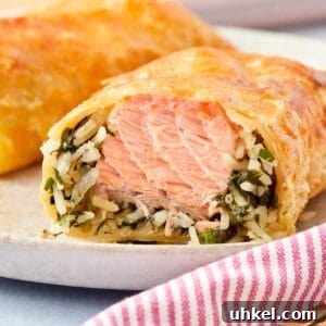 Close-up of a golden Puff Pastry Salmon Parcel sliced open to reveal flaky salmon, creamy spinach, and rice inside.