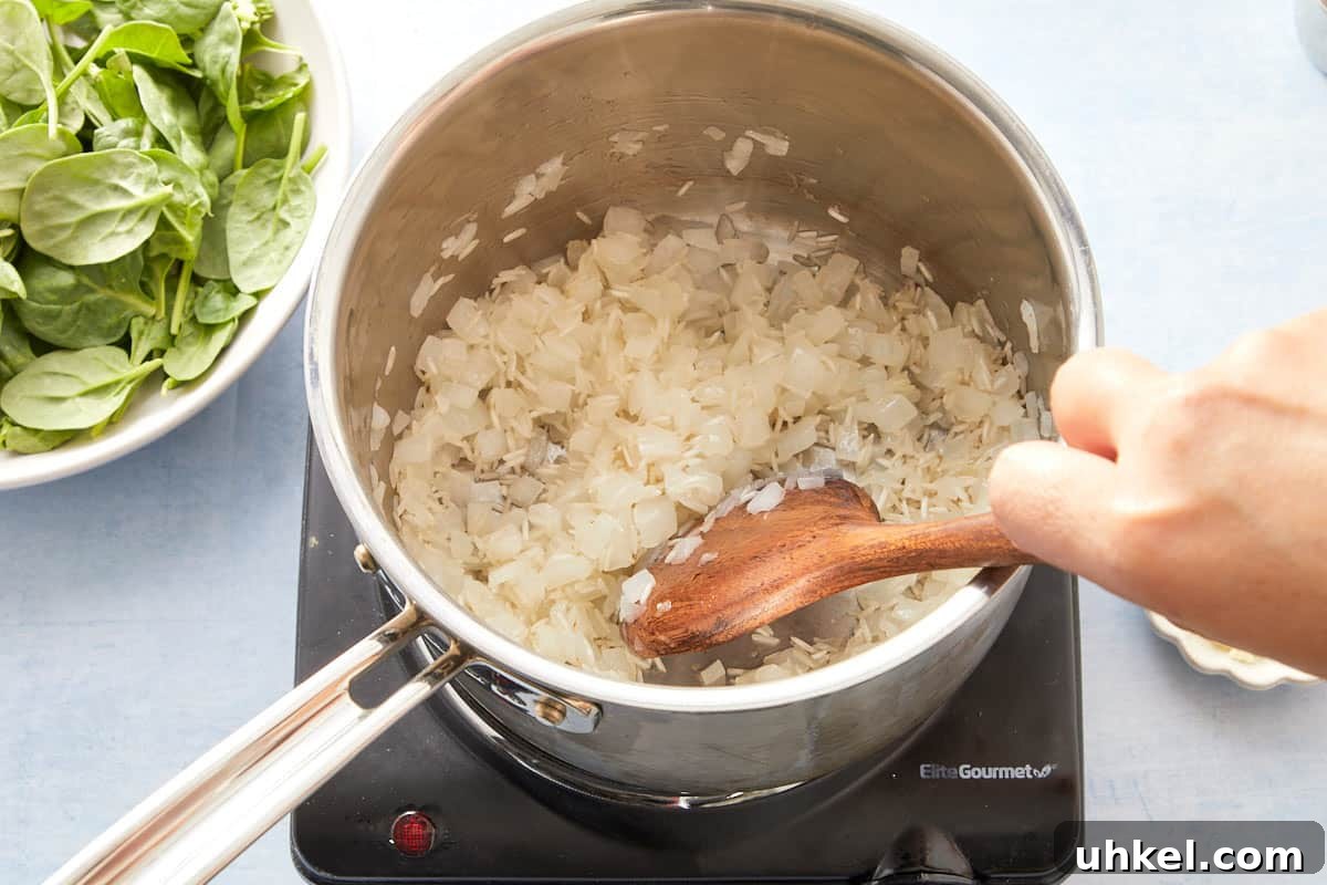 Stirring spinach and garlic into softened onions in a pot.