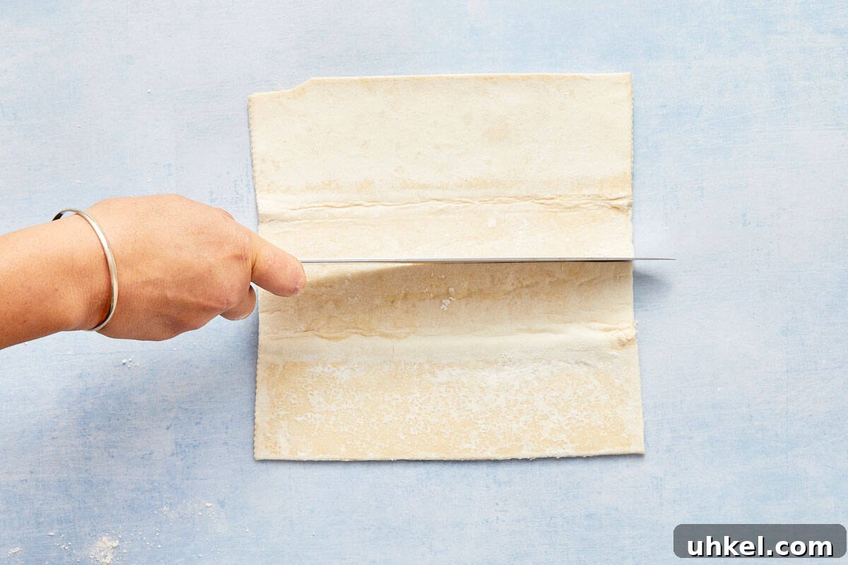 Puff pastry sheets being cut into rectangles on a light blue background.