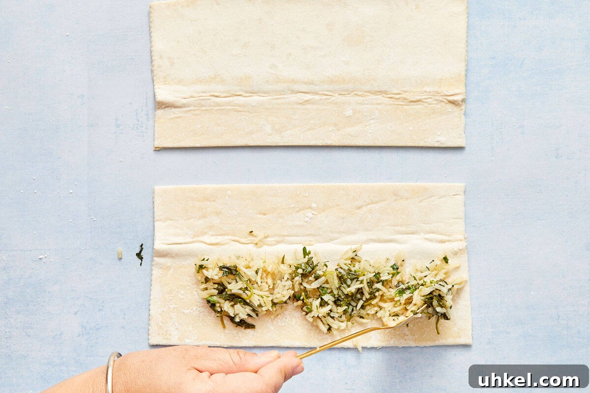 Spooning spinach and rice mixture onto the bottom half of the pastry sheet.