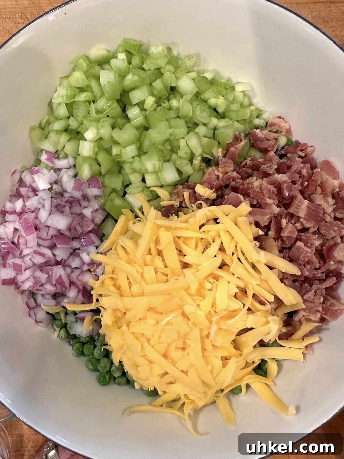 Creamy English Pea Salad with Bacon and Mint 5 Cheese, diced onion, bacon and celery in a large bowl on top of peas.
