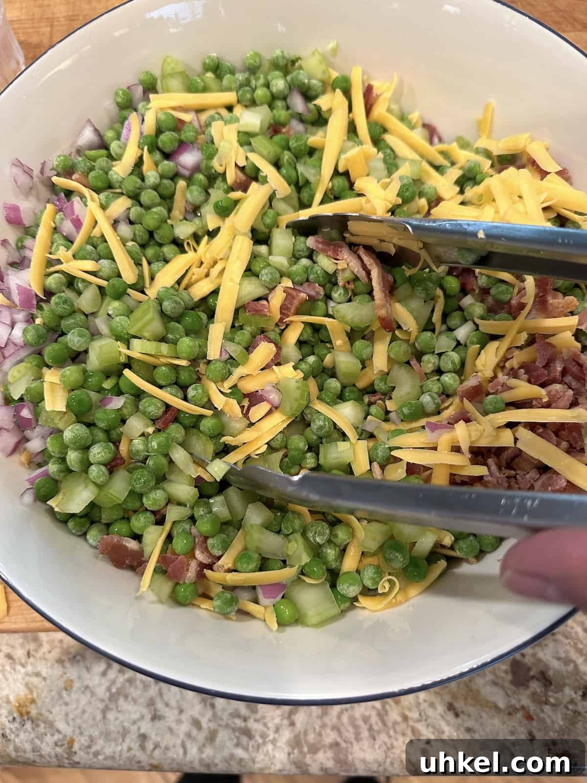 Creamy English Pea Salad with Bacon and Mint 6 Pea salad ingredients in a large bowl, tongs are stirring the ingredients.