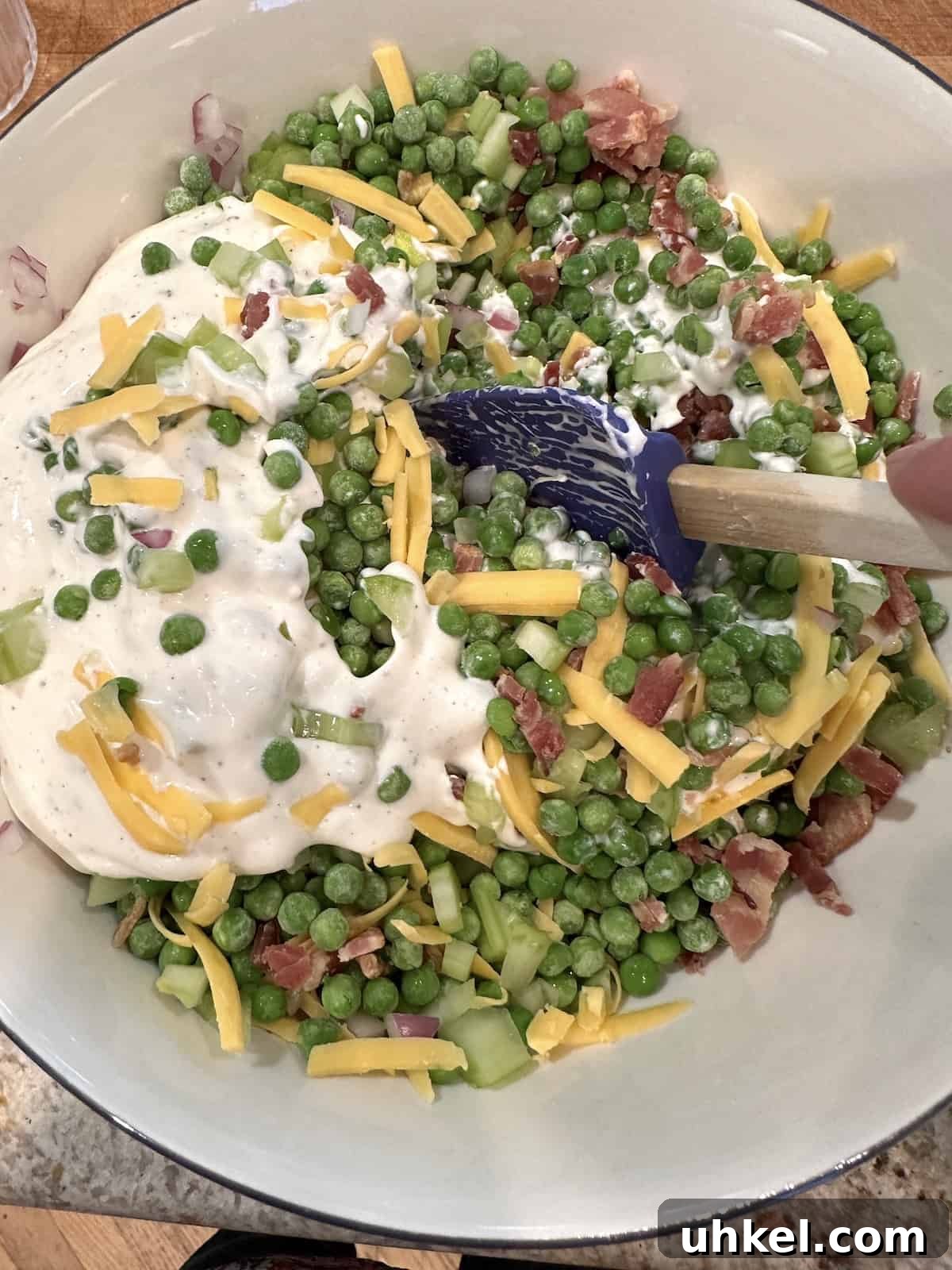 Creamy English Pea Salad with Bacon and Mint 7 Ingredients for pea salad in a bowl with the sauce placed on top but not fully blended yet.
