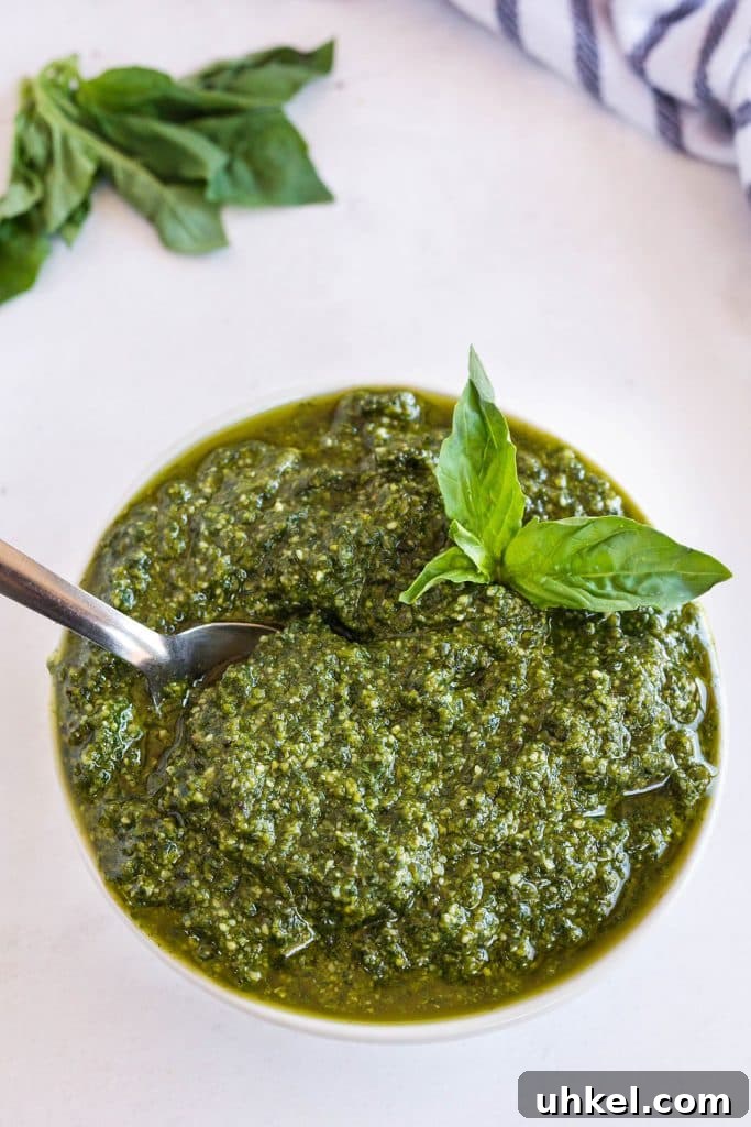 Classic Basil Pesto Recipe: Fresh, Vibrant Sauce for Pasta & More 2 Basil pesto sauce in a white bowl with a spoon and garnished with fresh basil.