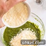 Classic Basil Pesto Recipe: Fresh, Vibrant Sauce for Pasta & More 17 pouring parmesan cheese into a bowl with pesto sauce