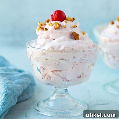 cherry salad topped with a cherry and chopped pecans in a mini glass parfait dish.