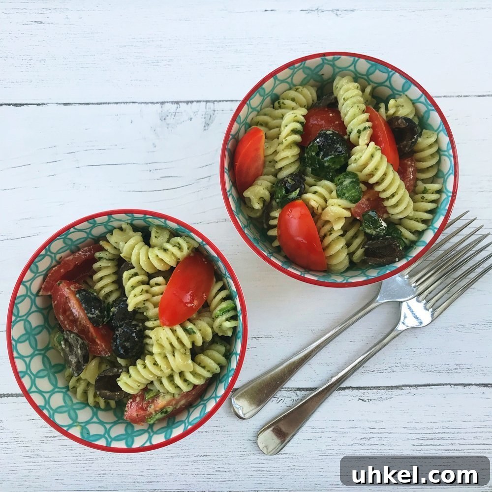 30-Minute Family Dinner Recipes Your Whole Family Will Love 8 white wooden table with two bowls of pasta pesto using fusilli pasta, homemade pesto, spinach, black olives and baby plum tomatoes