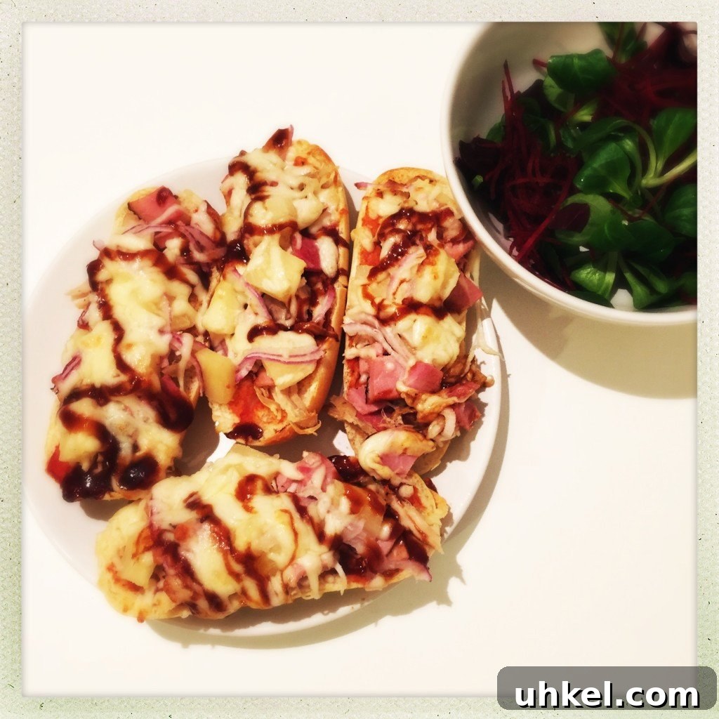 30-Minute Family Dinner Recipes Your Whole Family Will Love 13 A white plate with four french bread pizzas it, pizza topped with ham, cheese, pineapple and BBQ sauce, small white bowl of salad next to the plate