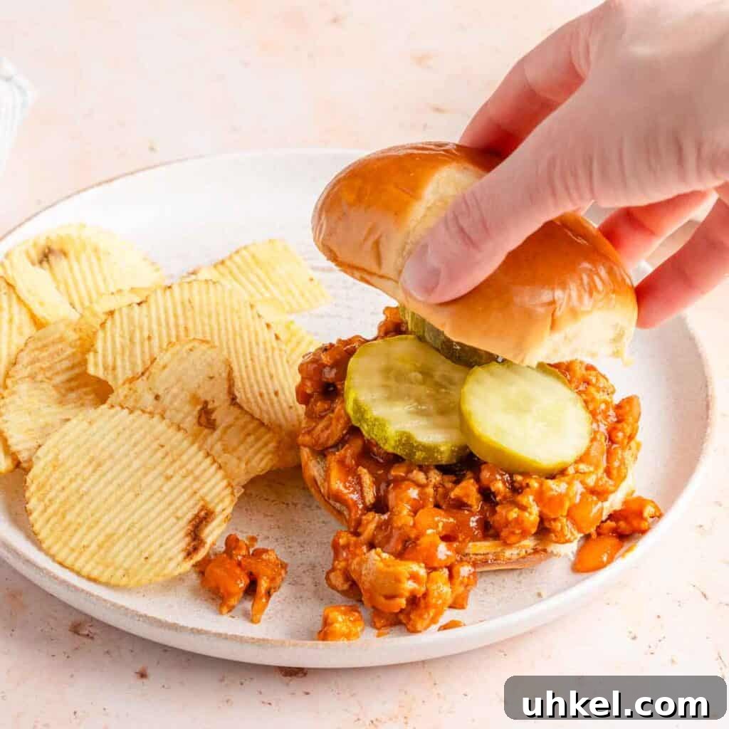 Ground Turkey-Style Sloppy Joes with Ground Chicken 7 hand adding bun top to sloppy Joe sandwich with chips on the side.