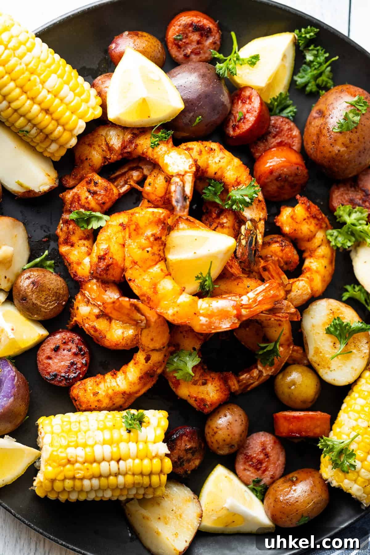 Smoked Shrimp Recipes: How to Smoke Shrimp Perfectly 2 Smoked shrimp on a black plate surrounded by corn, potatoes, and lemon slices.